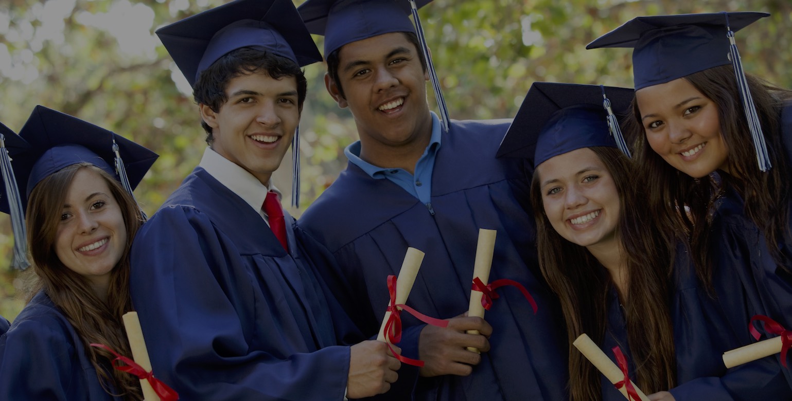 Graduating students smiling and laughing with diplomas; trees in background